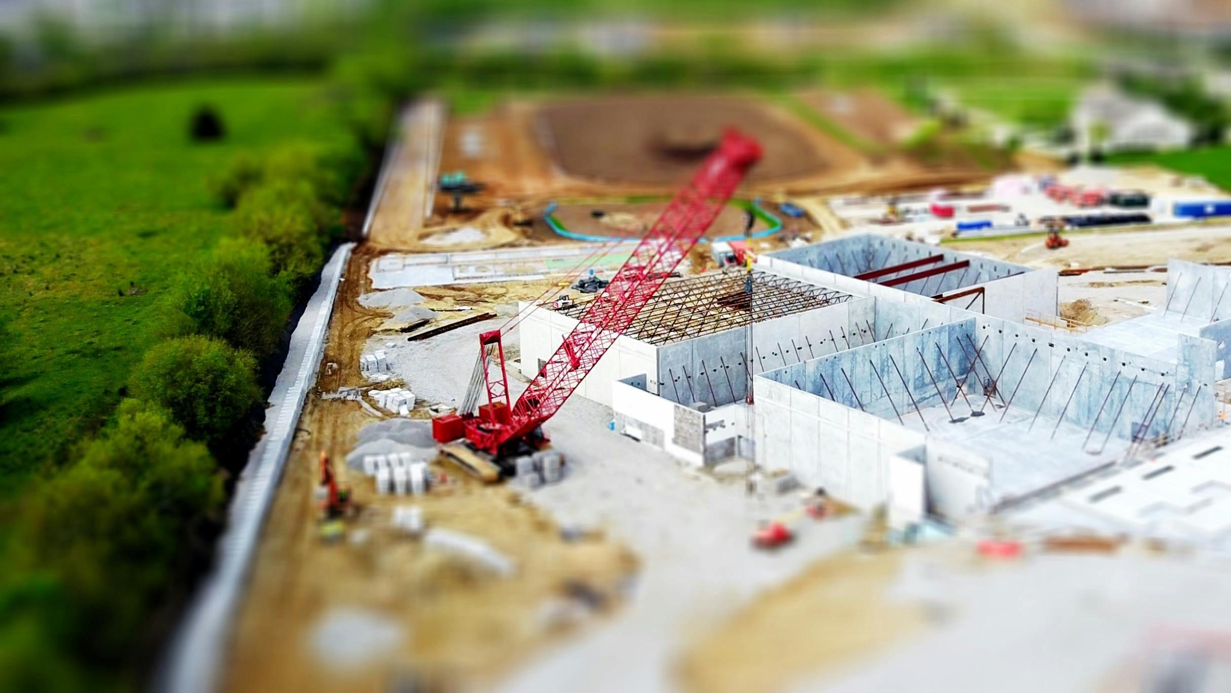 Baustelle mit rotem Mobilkran in Tilt-Shift-Optik, Betonfundament mit Bewehrungsstahl im Bau